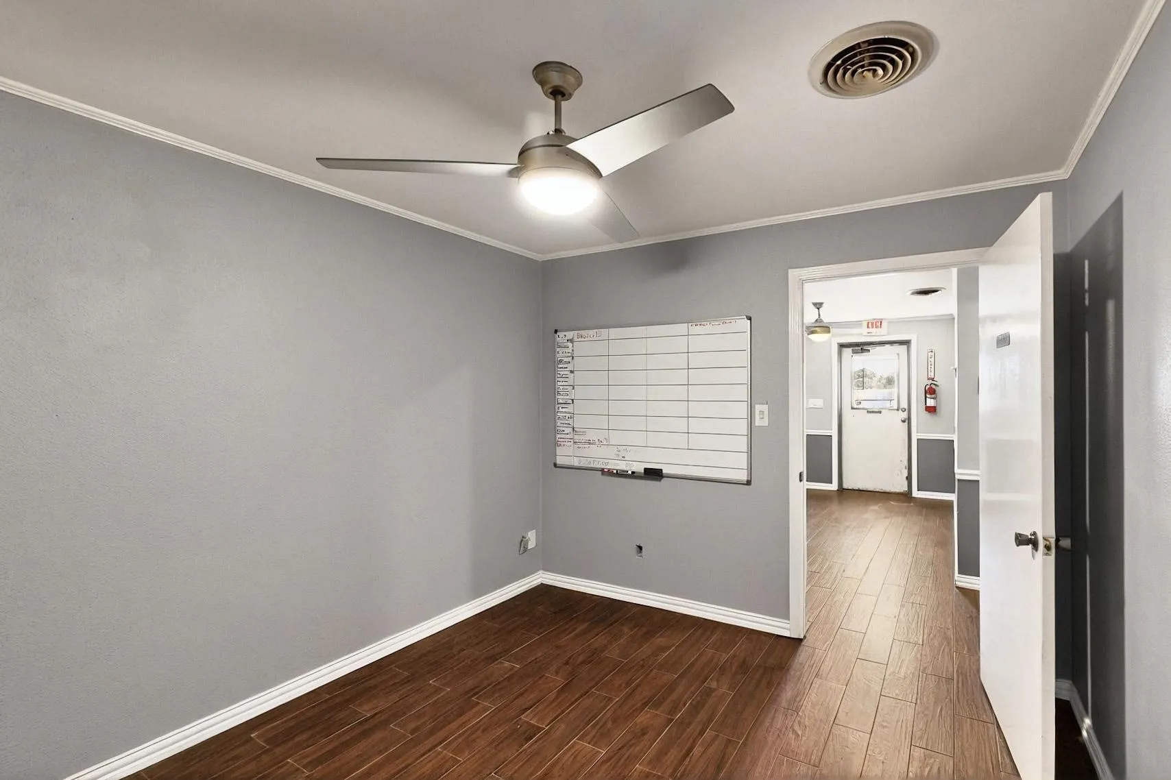 Empty room featuring ceiling fan, dark wood finished floors, crown molding, and baseboards