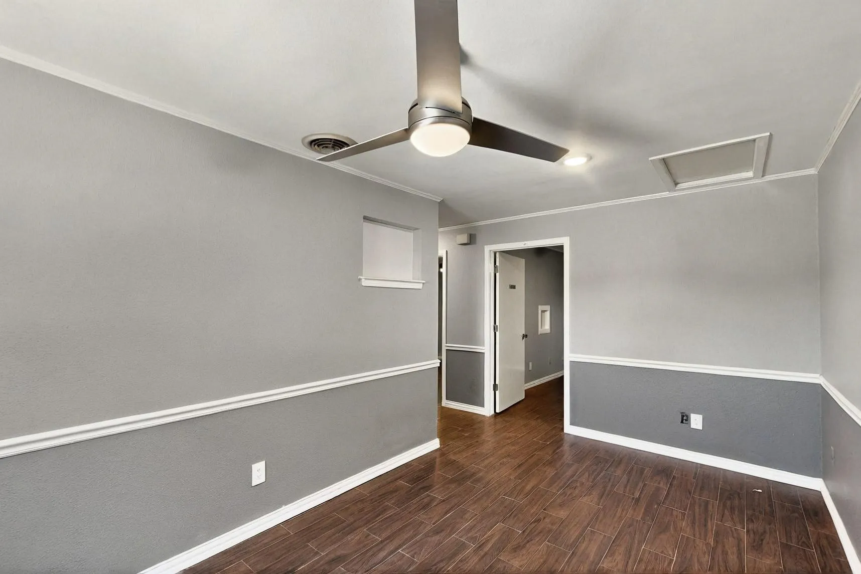 Empty room featuring ornamental molding, baseboards, wood finished floors, a ceiling fan, and attic access