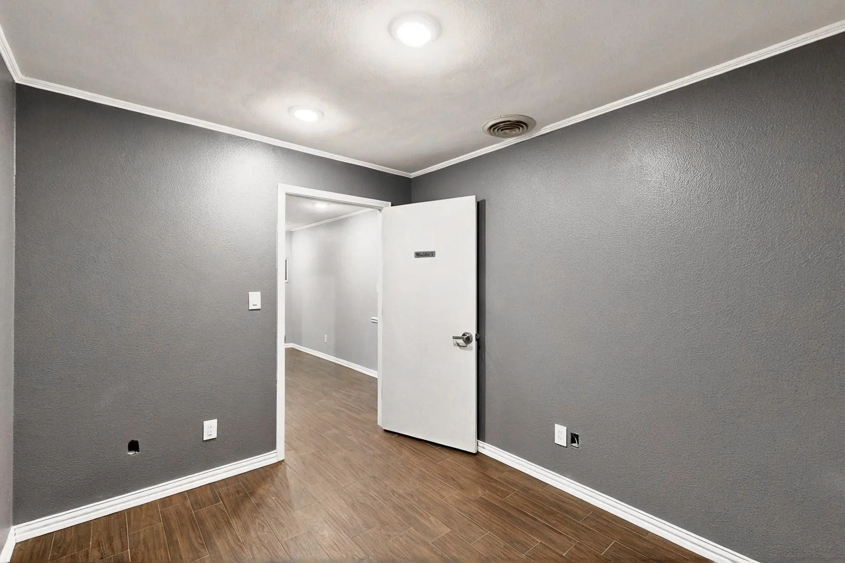 Empty room featuring wood finished floors, baseboards, and crown molding