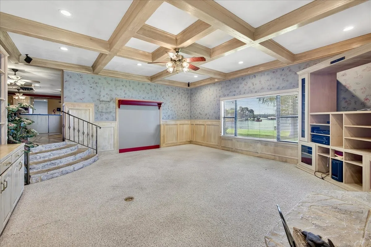 Unfurnished living room featuring ceiling fan, carpet, beam ceiling, coffered ceiling, and wallpapered walls