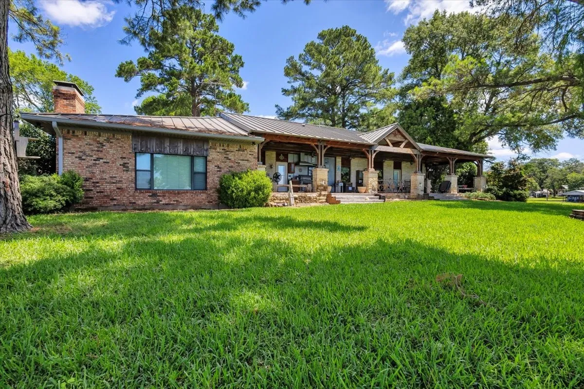 Back of property featuring a lawn, brick siding, a chimney, a standing seam roof, and covered porch