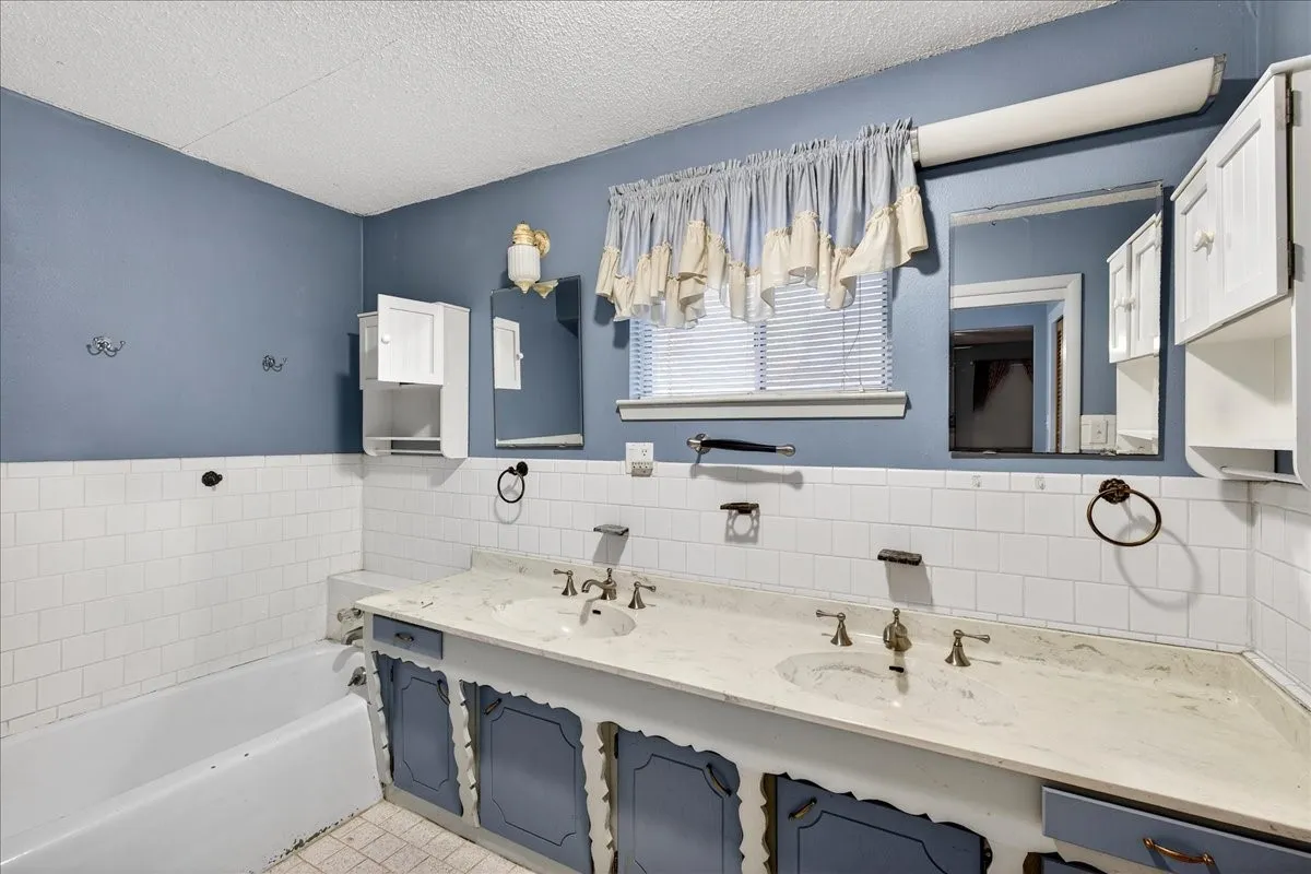Bathroom featuring tile walls, double vanity, a bath, a textured ceiling, and a wainscoted wall