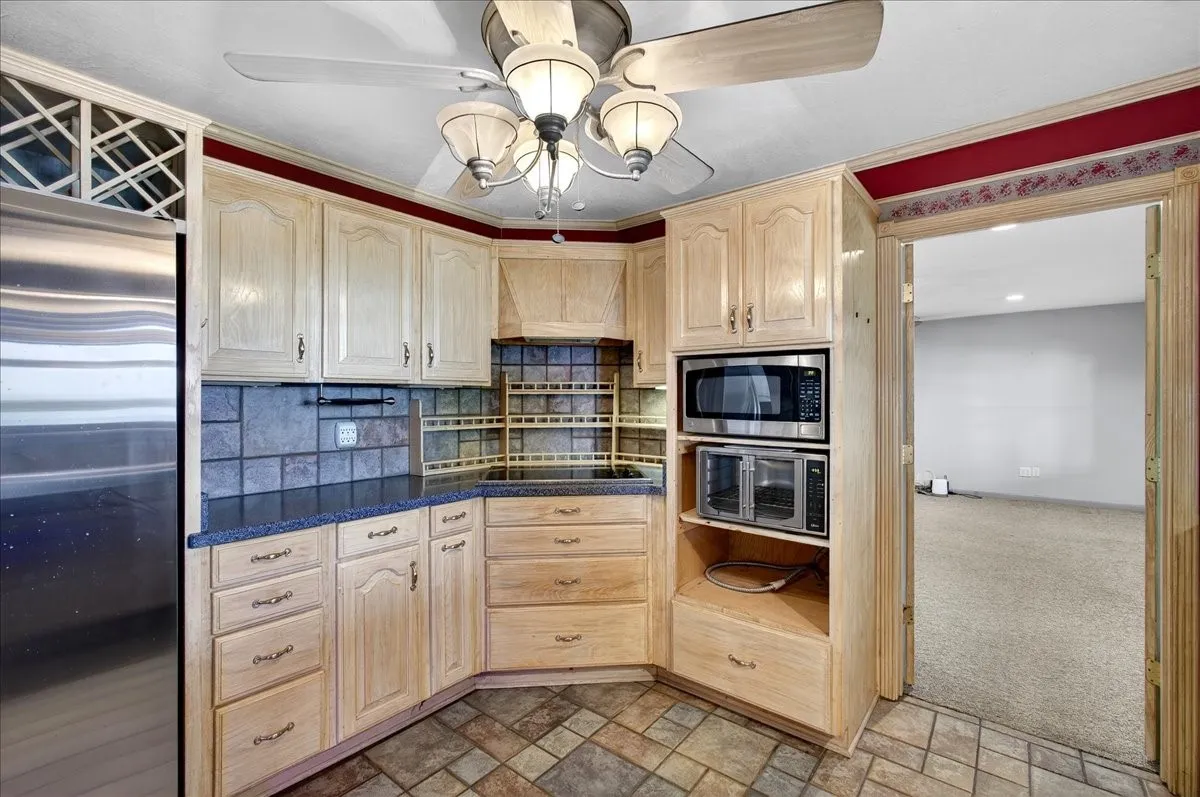 Kitchen with appliances with stainless steel finishes, light brown cabinets, ceiling fan, dark countertops, and backsplash
