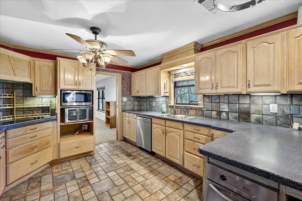 Kitchen featuring stainless steel appliances, light brown cabinetry, and dark countertops