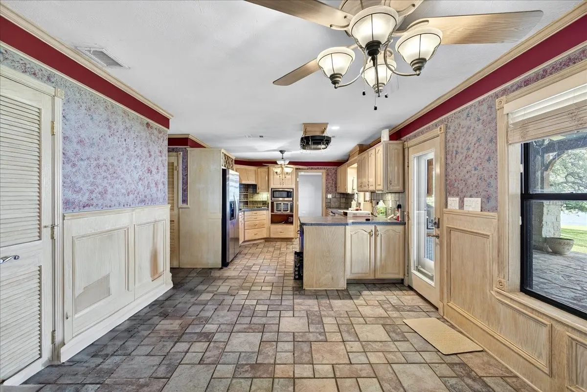 Kitchen featuring appliances with stainless steel finishes, a peninsula, wallpapered walls, light brown cabinetry, and wainscoting