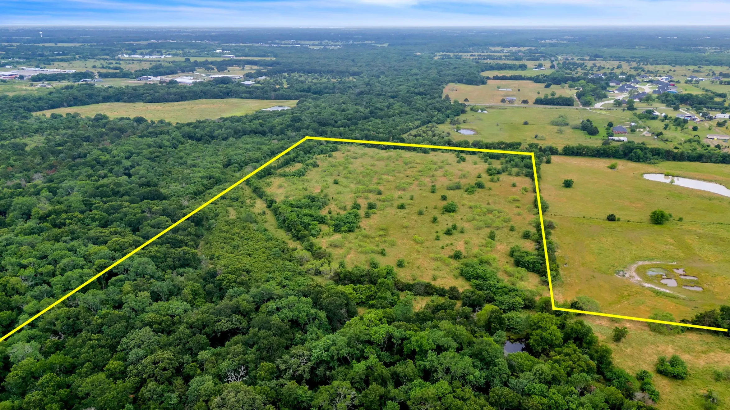 Aerial view of property's location with property parcel outlined, a forest, and a nearby body of water