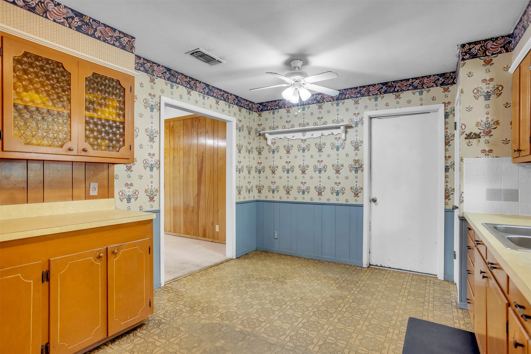 Kitchen with wallpapered walls, wainscoting, light countertops, ceiling fan, and light flooring
