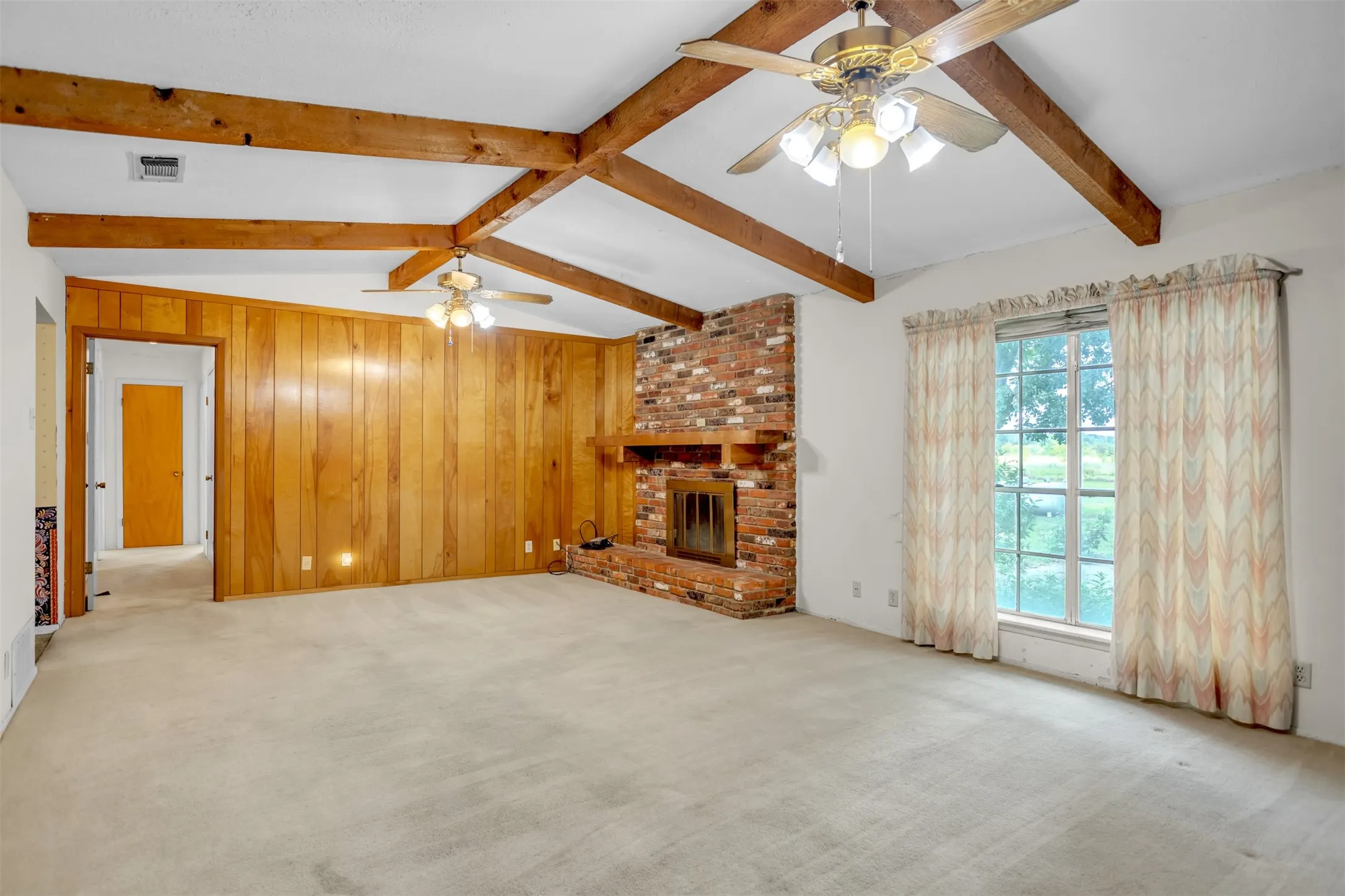 Unfurnished living room with a ceiling fan, carpet, a brick fireplace, and wood walls