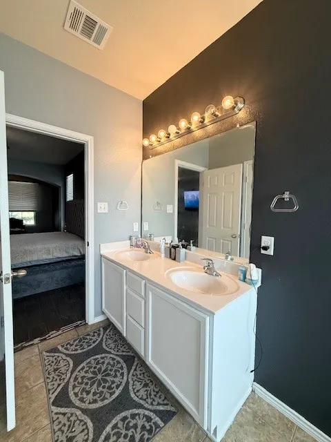 Full bathroom with ensuite bath, double vanity, tile patterned flooring, and baseboards