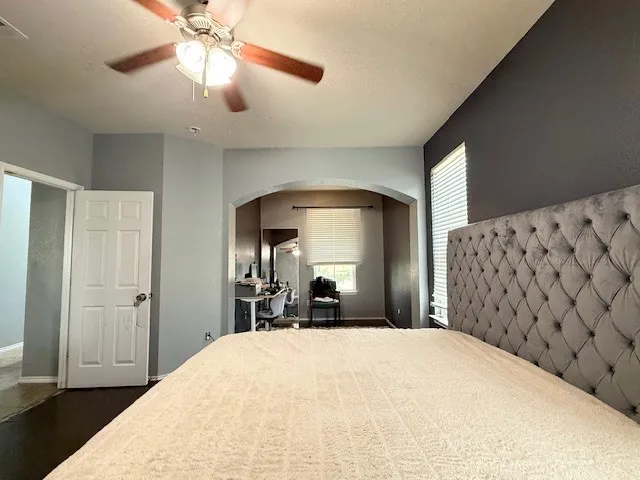 Bedroom with arched walkways, multiple windows, dark wood-style flooring, and a ceiling fan