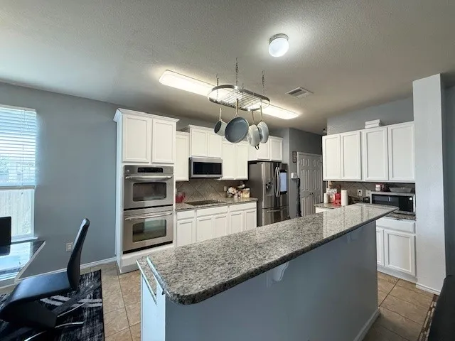 Kitchen with stainless steel appliances, tasteful backsplash, light tile patterned flooring, white cabinets, and a textured ceiling
