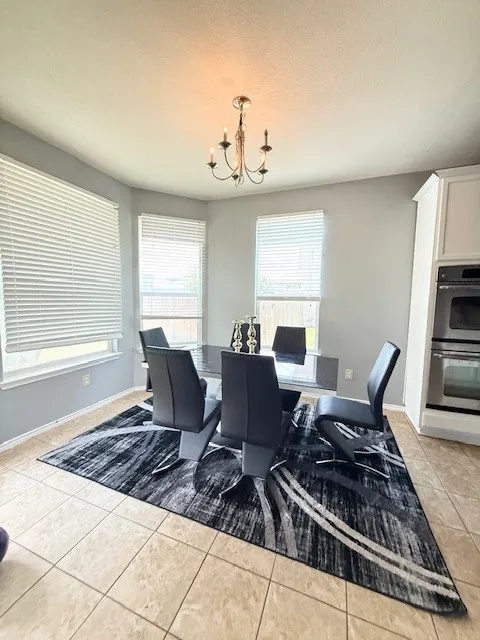 Dining space with a chandelier, light tile patterned floors, and baseboards
