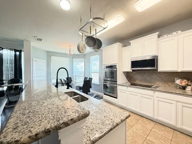 Kitchen with appliances with stainless steel finishes, a sink, decorative backsplash, white cabinetry, and a large island