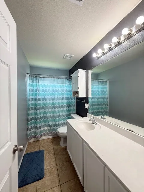 Bathroom with vanity, toilet, tile patterned flooring, a textured ceiling, and a shower with shower curtain