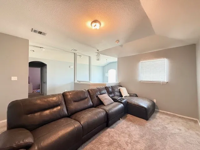 Carpeted living area with arched walkways, a textured ceiling, and baseboards