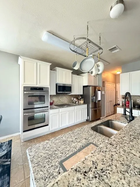 Kitchen featuring stainless steel appliances, a sink, tasteful backsplash, white cabinetry, and a textured ceiling