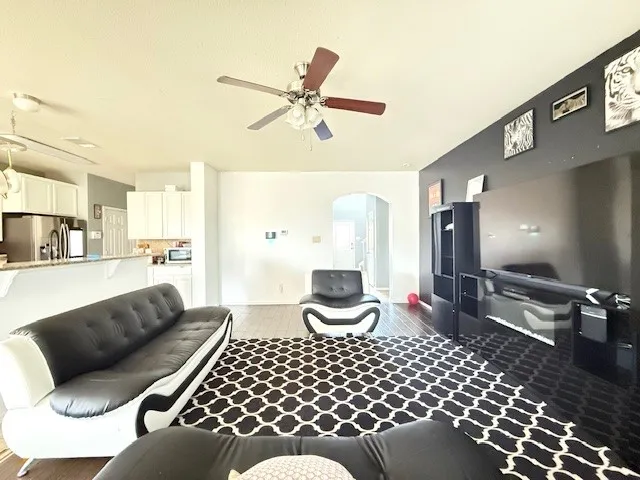 Living area with a ceiling fan, arched walkways, wood finished floors, and baseboards