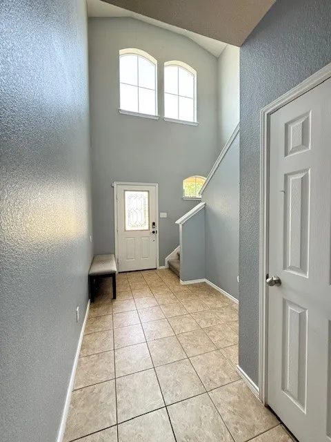 Entryway with a textured wall, light tile patterned floors, stairway, a high ceiling, and baseboards