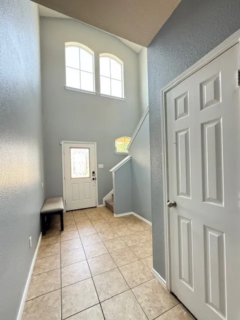 Foyer featuring a towering ceiling, a textured wall, light tile patterned floors, stairs, and baseboards