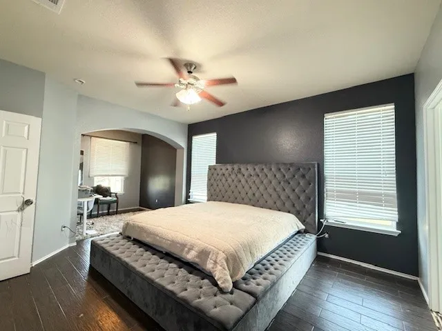 Bedroom featuring arched walkways, baseboards, and dark wood-style flooring
