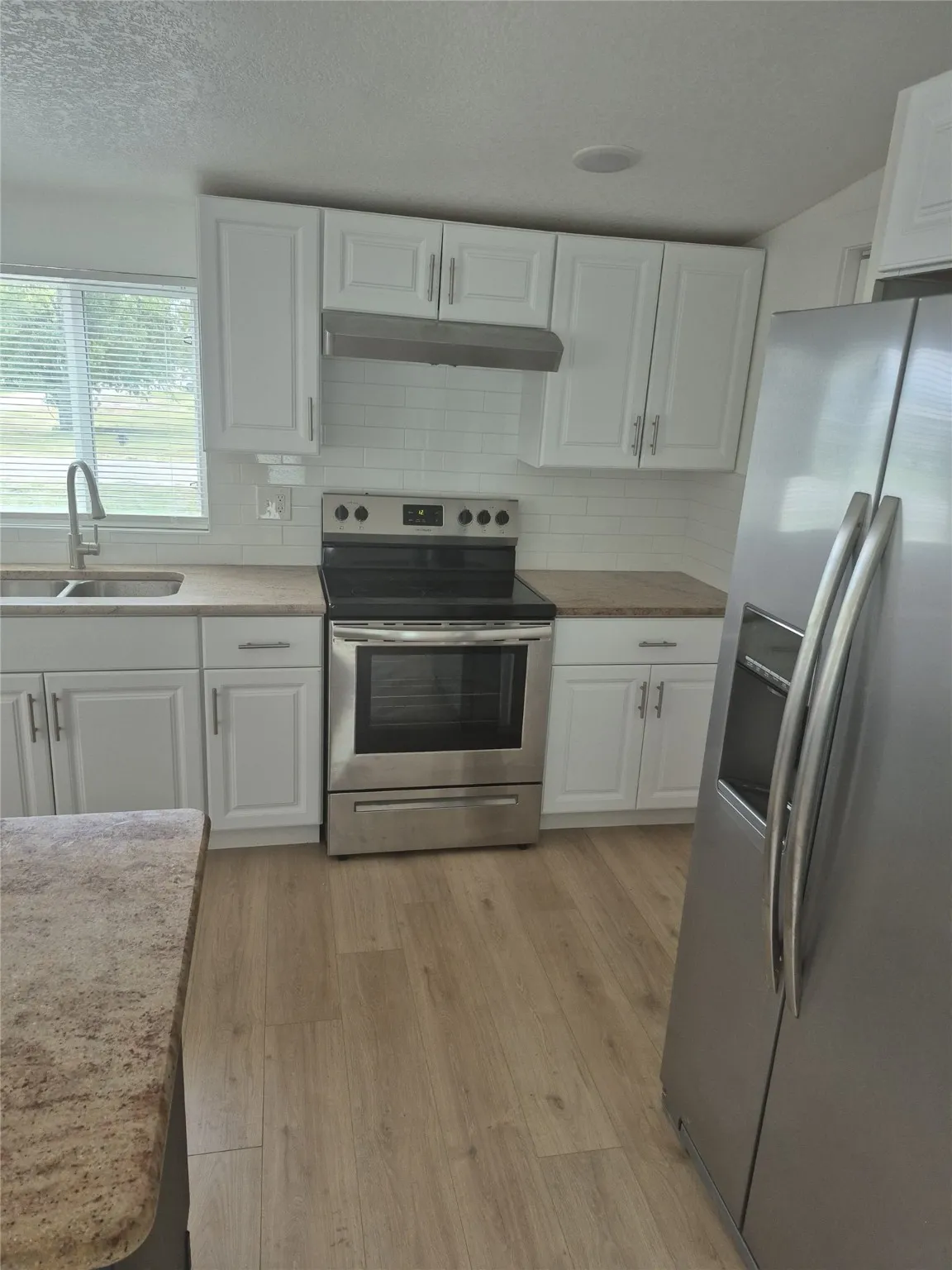 Kitchen featuring appliances with stainless steel finishes, white cabinets, tasteful backsplash, under cabinet range hood, and a textured ceiling
