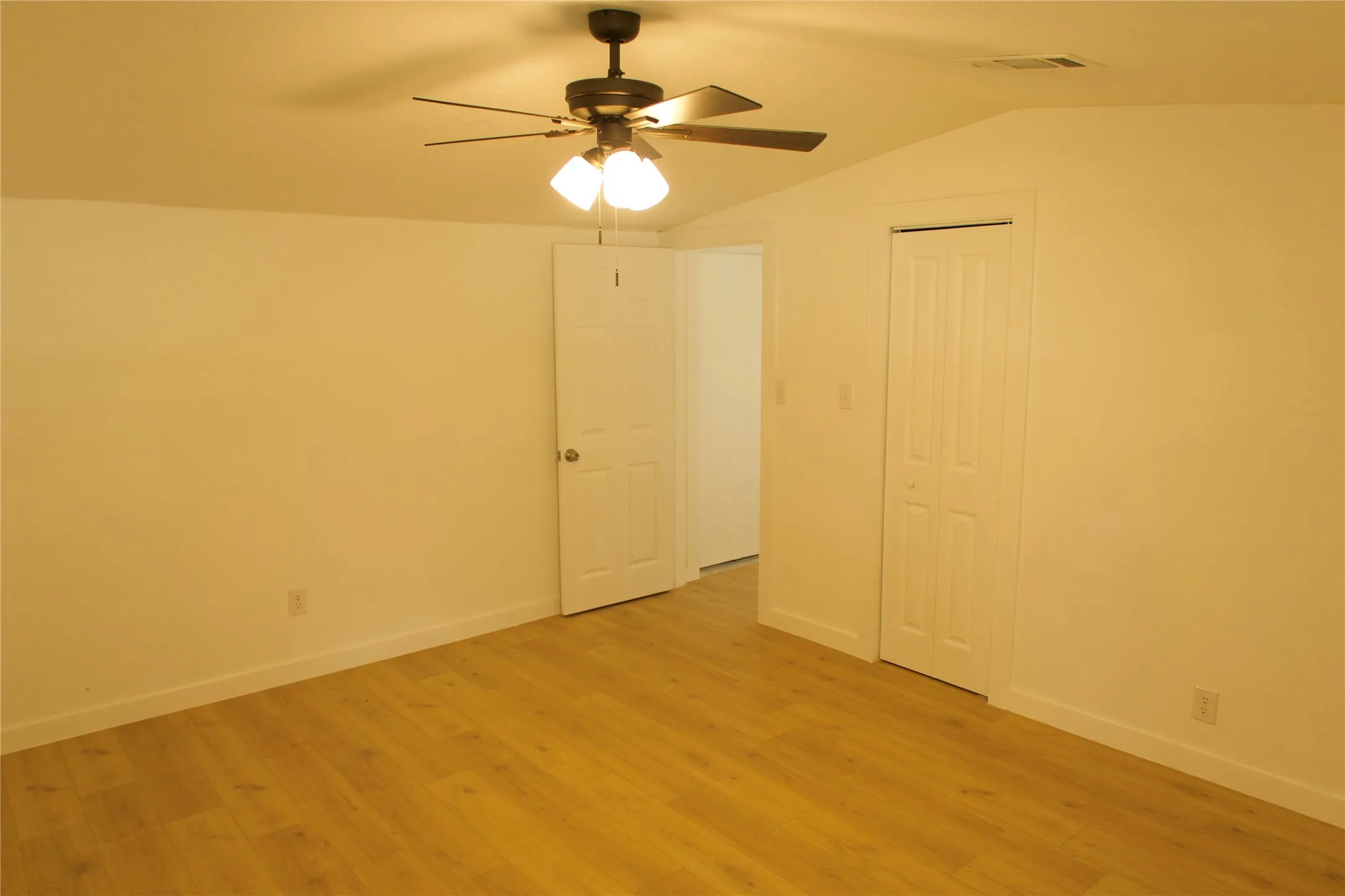 Unfurnished bedroom featuring light wood-type flooring, vaulted ceiling, a closet, and baseboards