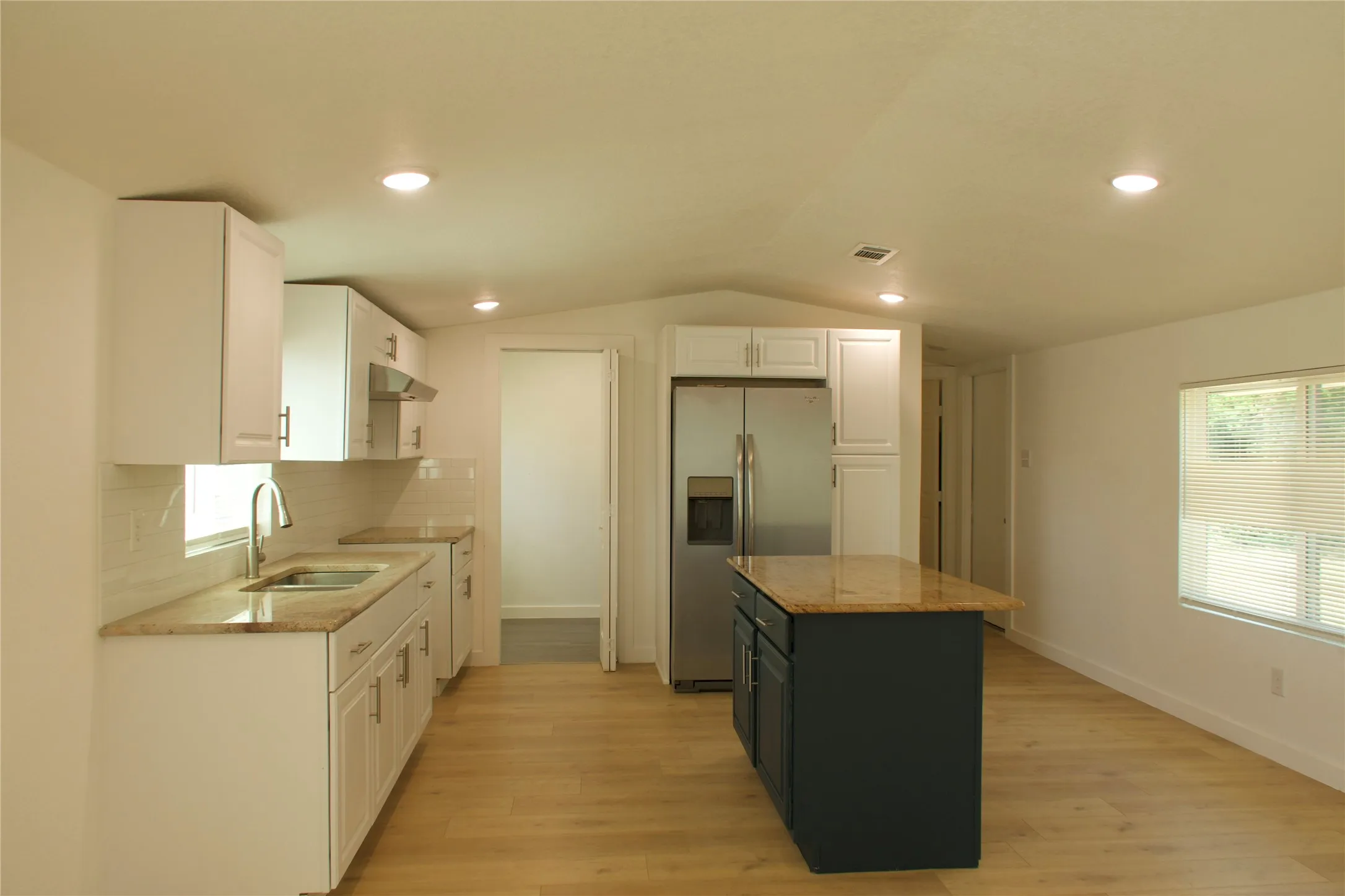 Kitchen with stainless steel fridge, a sink, under cabinet range hood, white cabinets, and light wood-type flooring