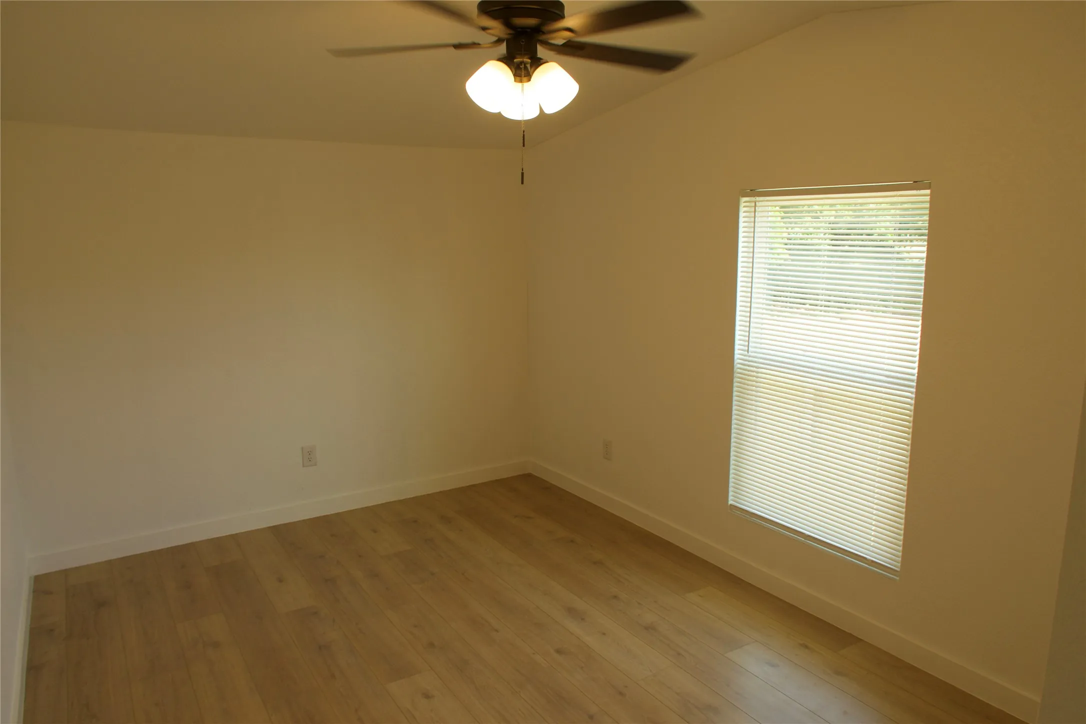 Spare room with lofted ceiling, ceiling fan, light wood-style flooring, and baseboards