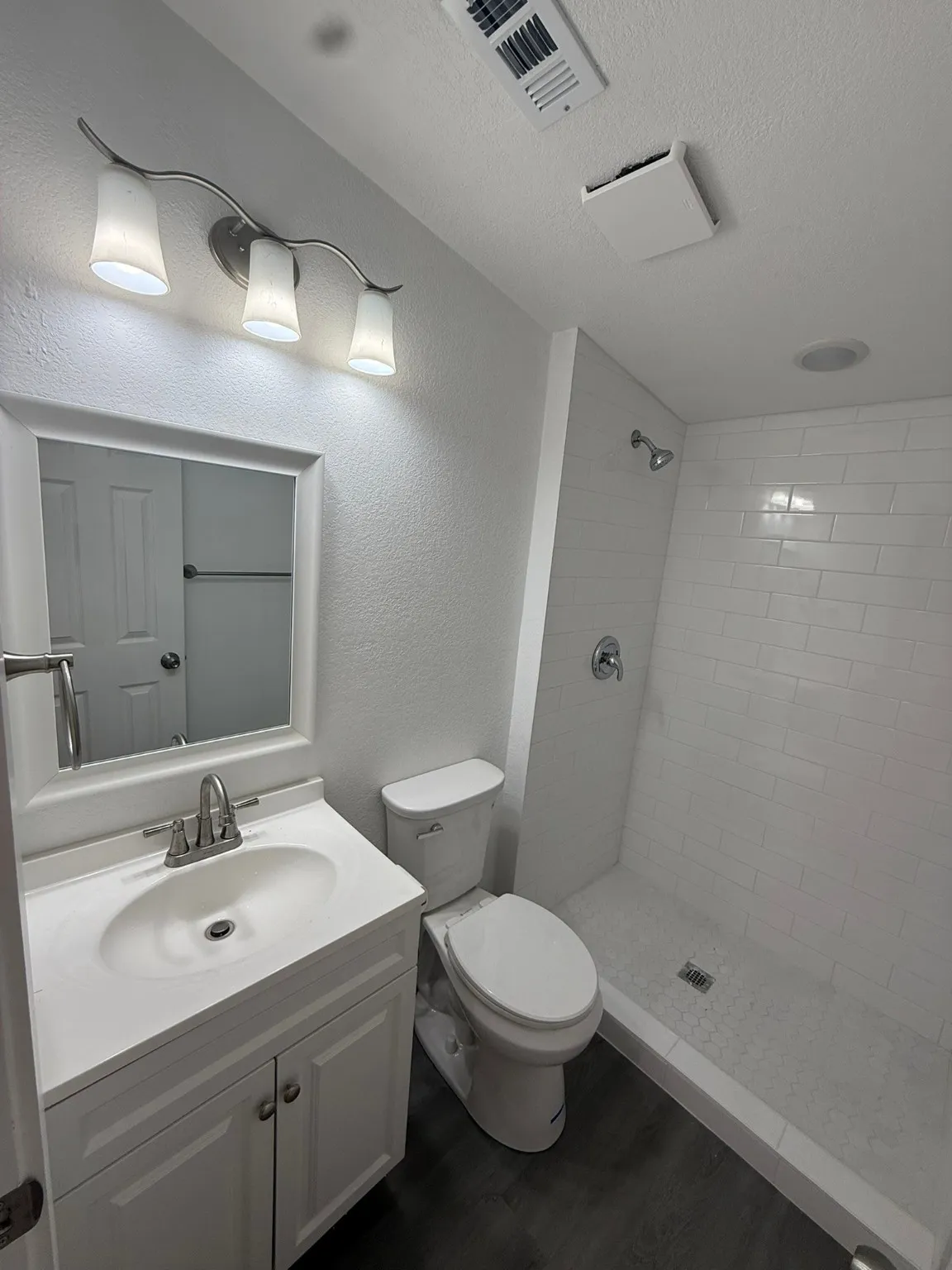 Full bathroom featuring a tile shower, vanity, a textured ceiling, toilet, and wood finished floors