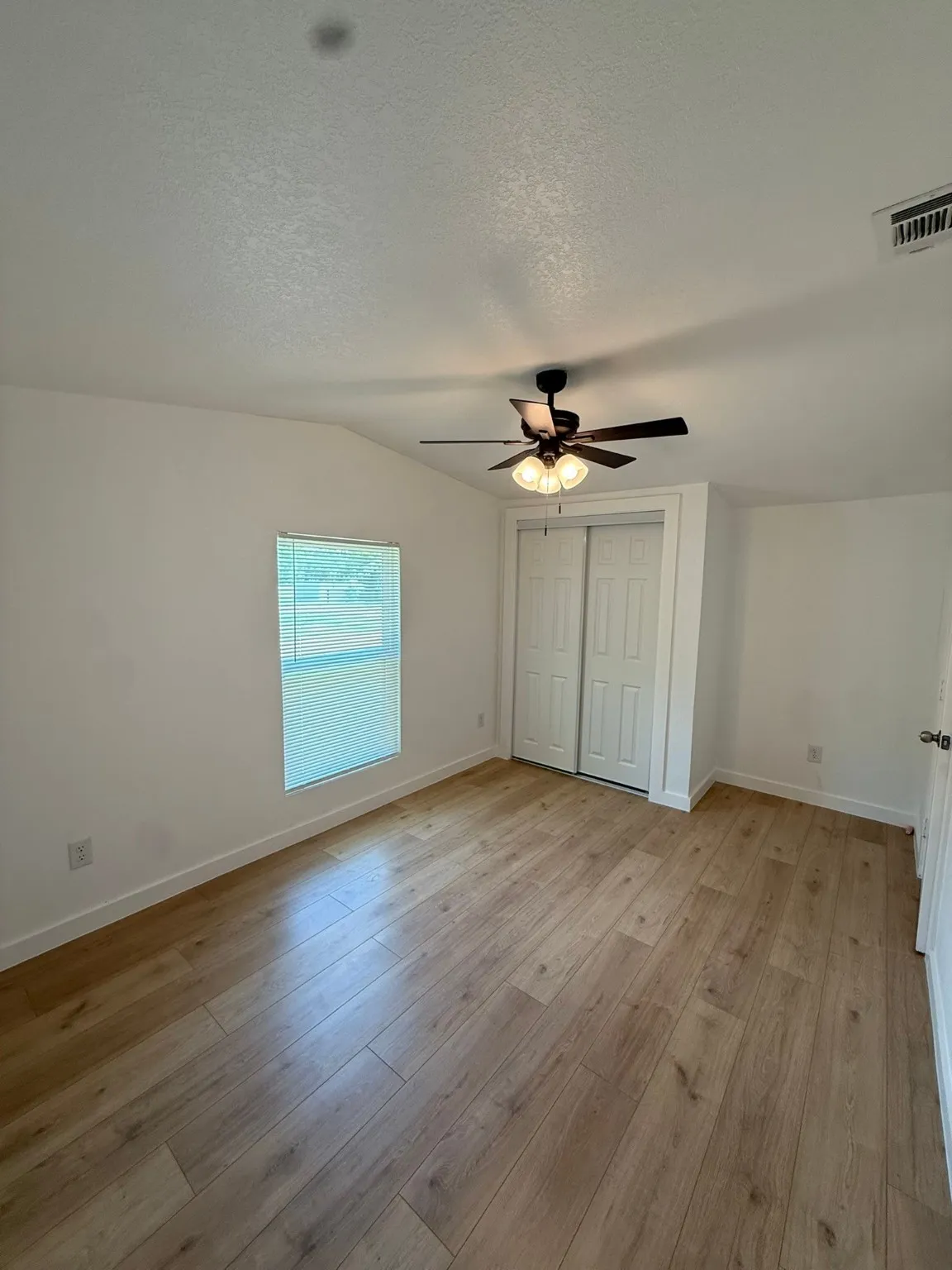Unfurnished bedroom featuring light wood-style flooring, lofted ceiling, a textured ceiling, baseboards, and a ceiling fan