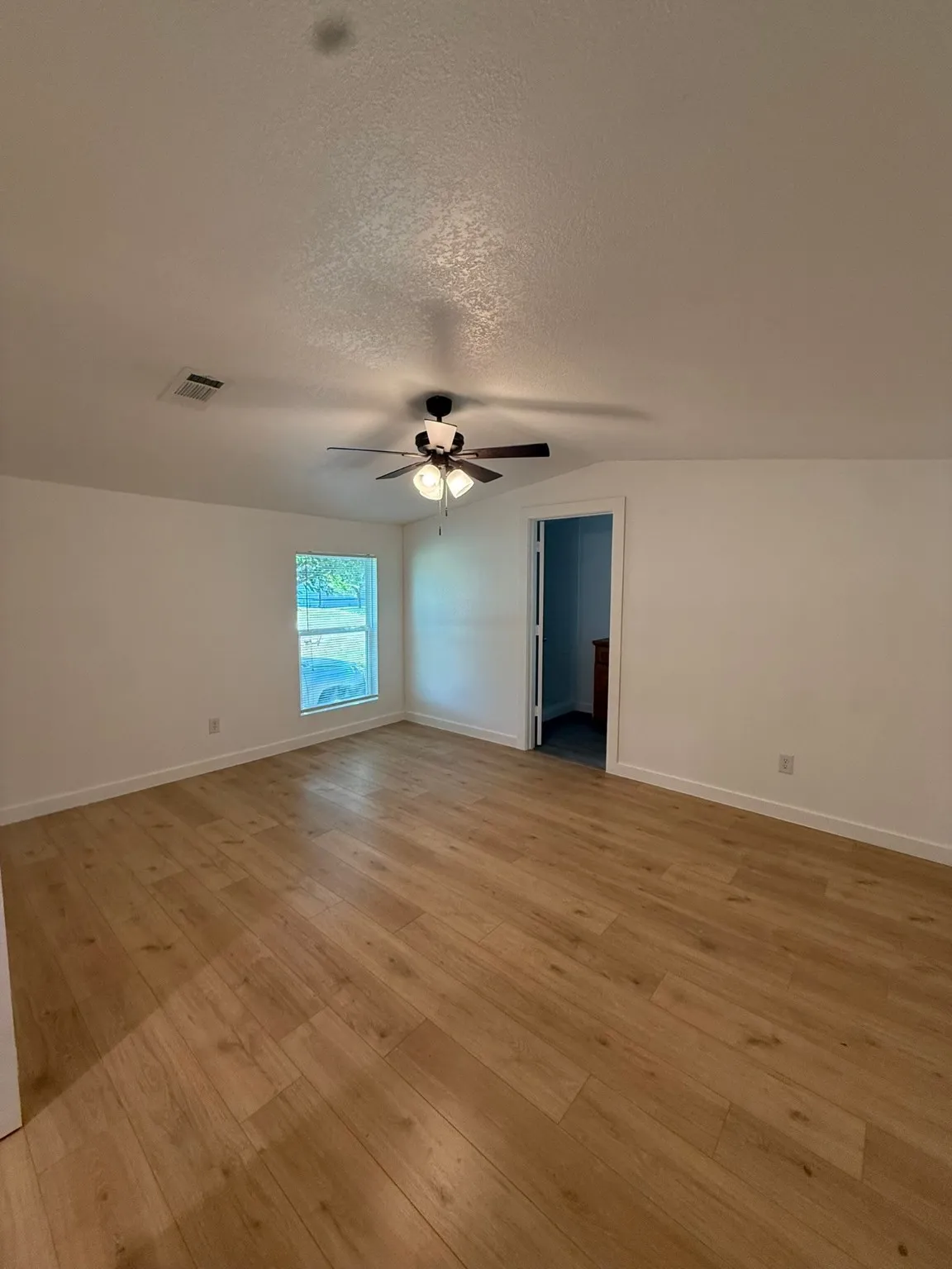 Empty room with light wood-type flooring, a ceiling fan, a textured ceiling, and baseboards