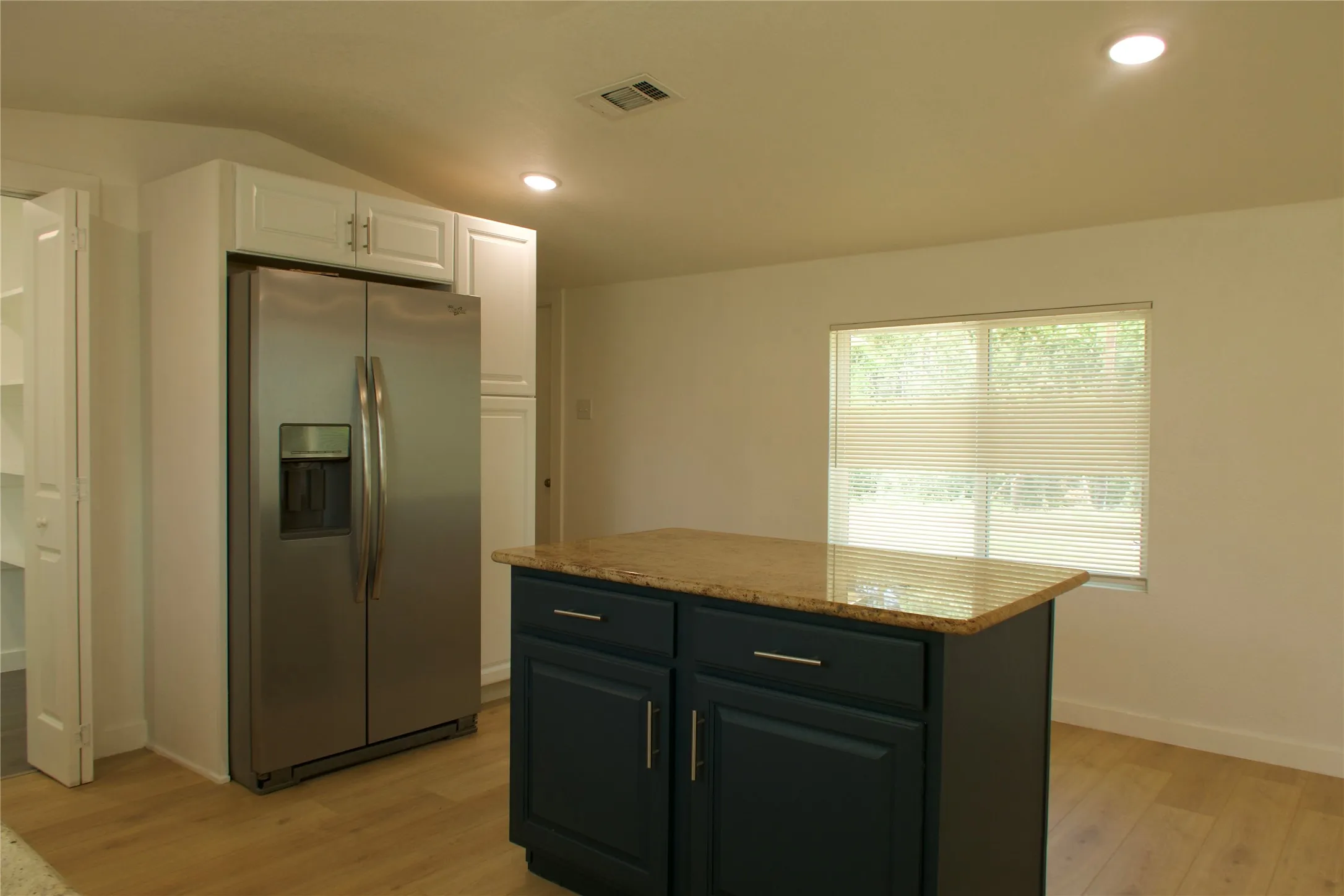 Kitchen featuring stainless steel fridge with ice dispenser, light wood-style flooring, white cabinetry, a center island, and baseboards