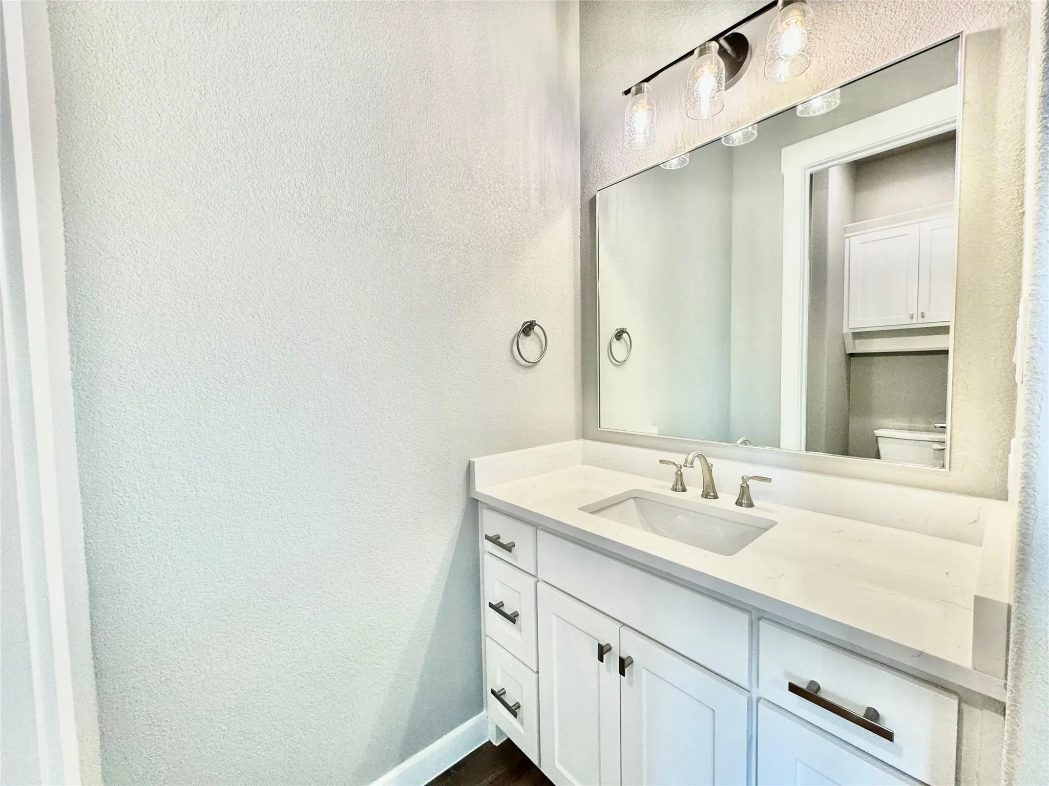 Bathroom featuring a textured wall, vanity, toilet, baseboards, and wood finished floors