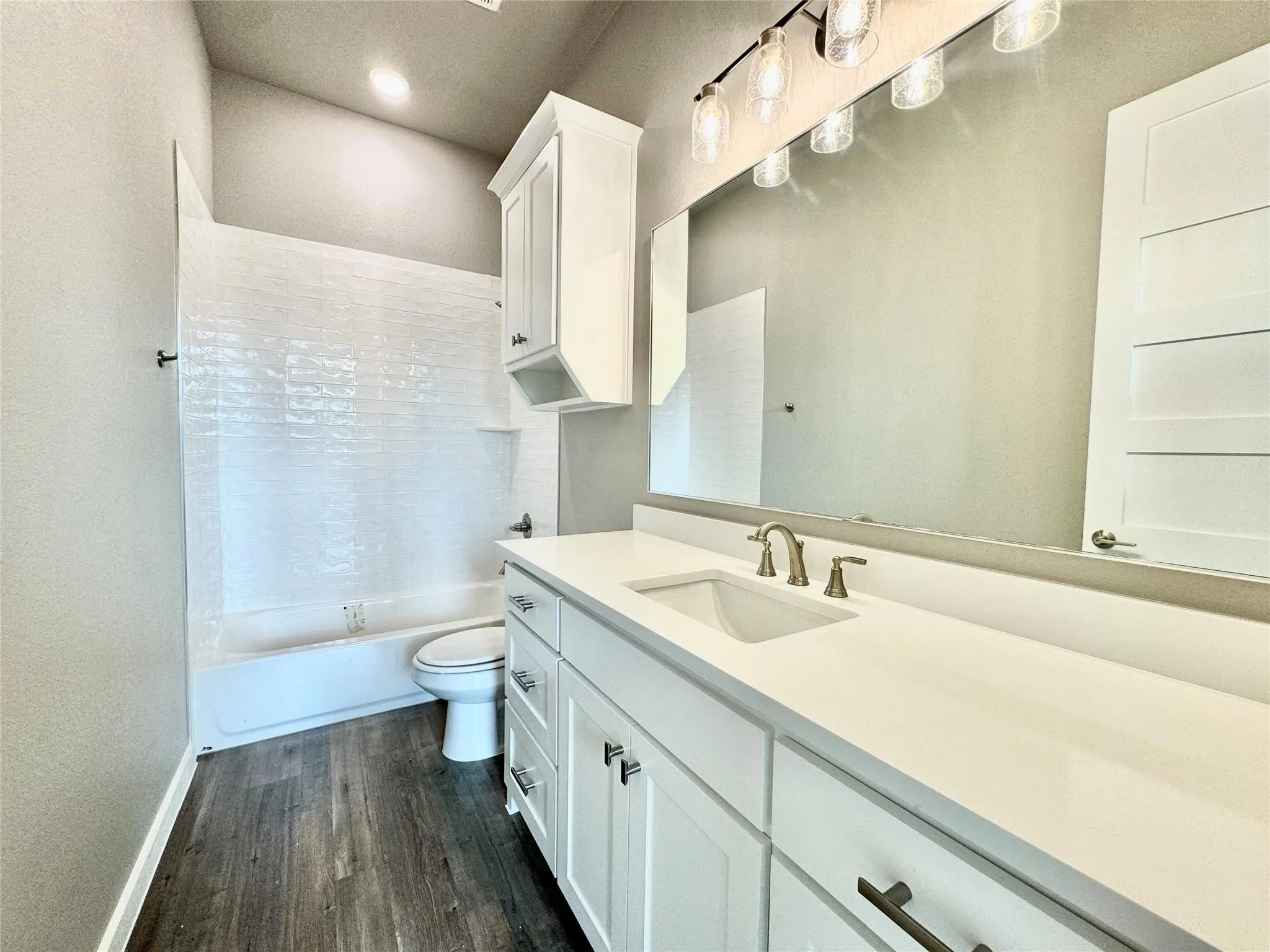 Bathroom featuring vanity, wood finished floors, toilet, shower / bathtub combination, and recessed lighting