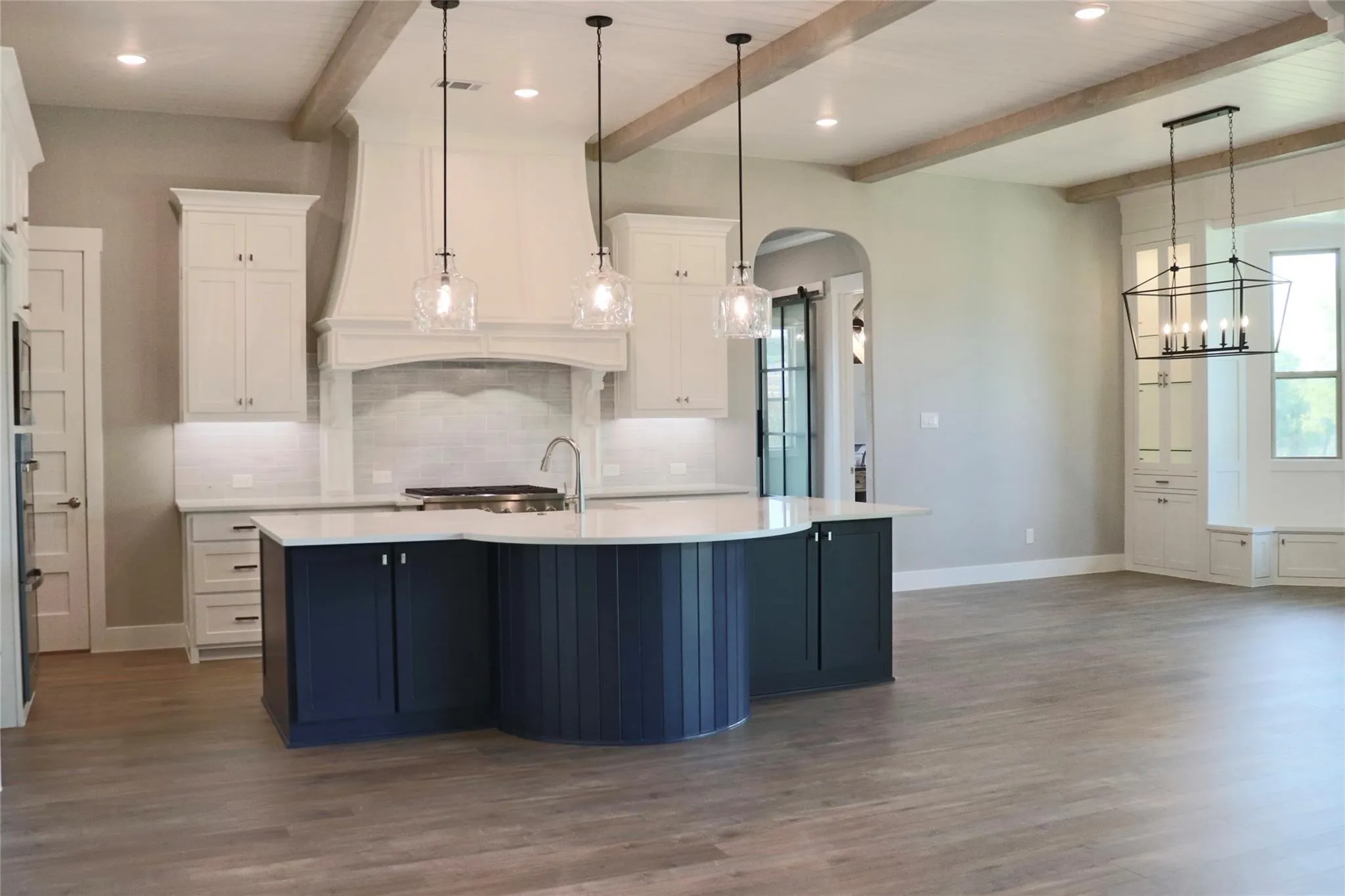Kitchen with arched walkways, light countertops, baseboards, beamed ceiling, and decorative backsplash
