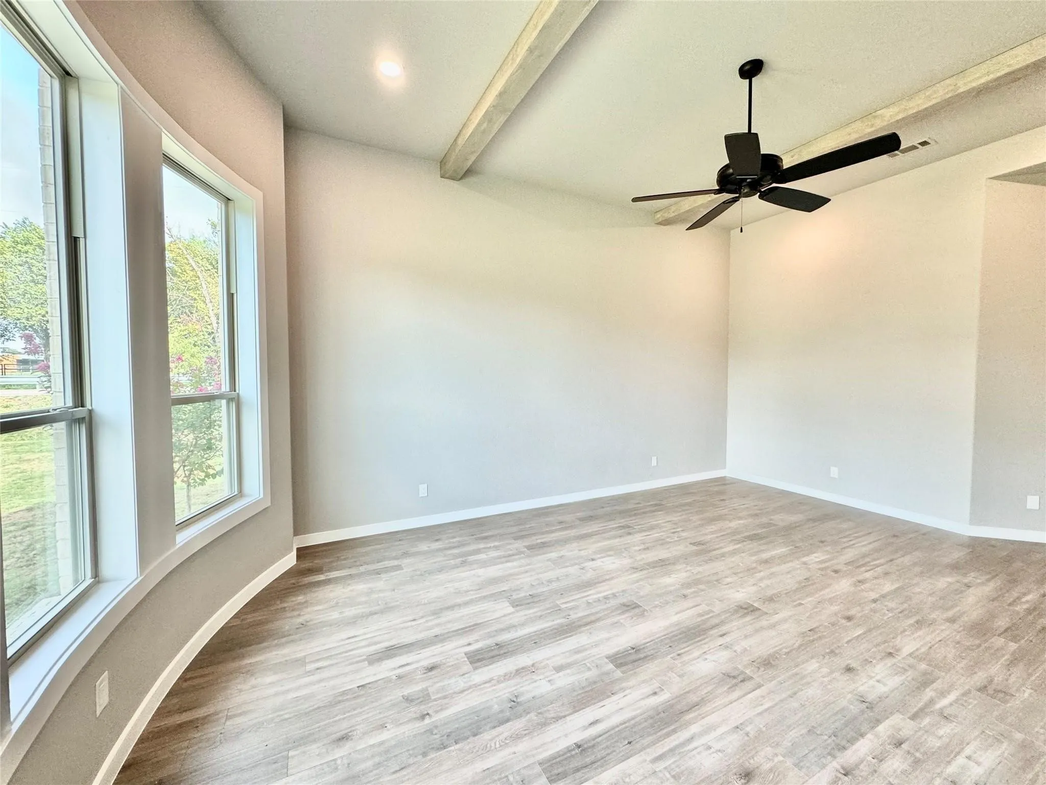 Unfurnished room featuring healthy amount of natural light, beam ceiling, wood finished floors, and baseboards