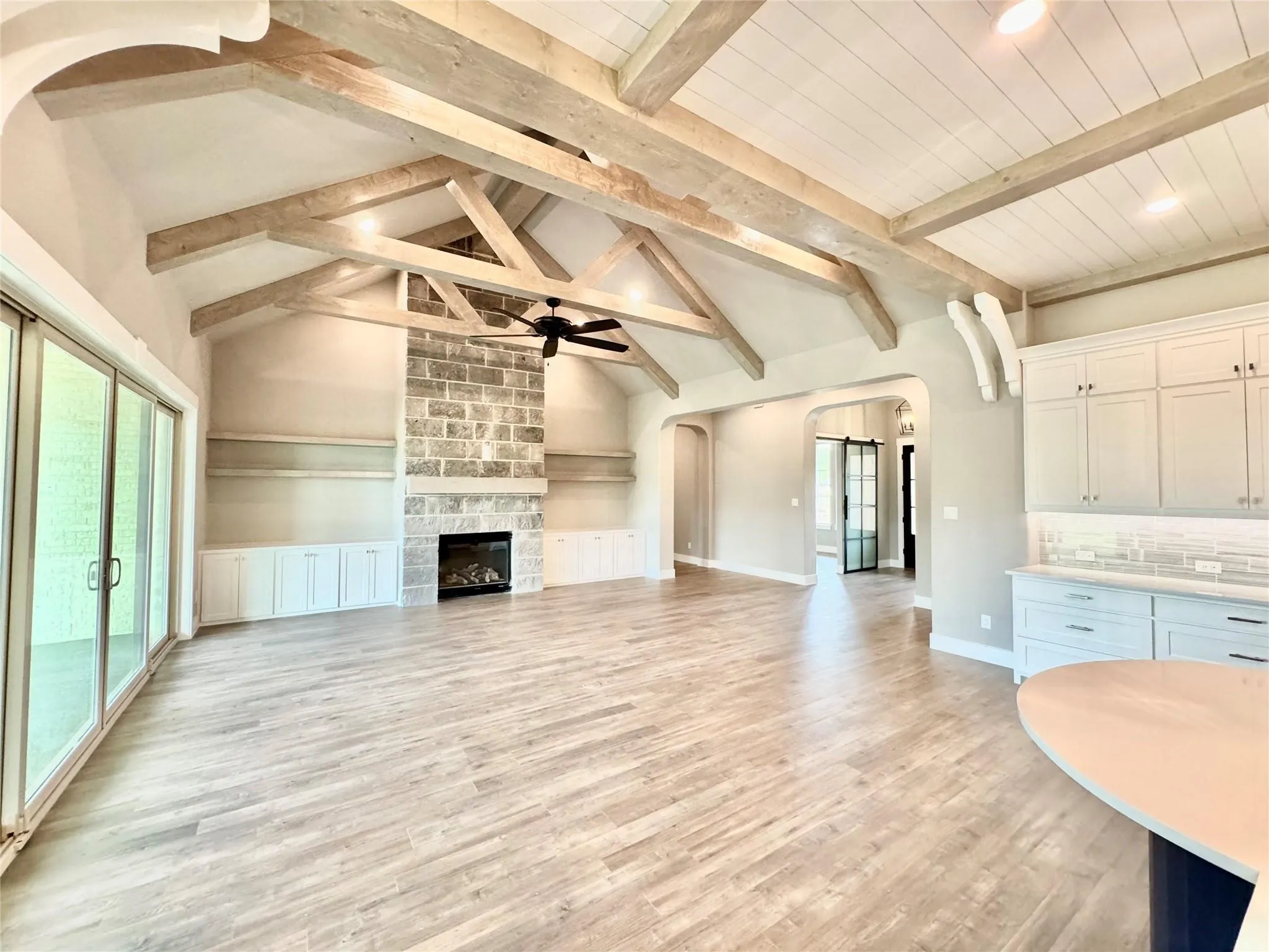 Unfurnished living room featuring arched walkways, ceiling fan, healthy amount of natural light, beam ceiling, and light wood-style floors