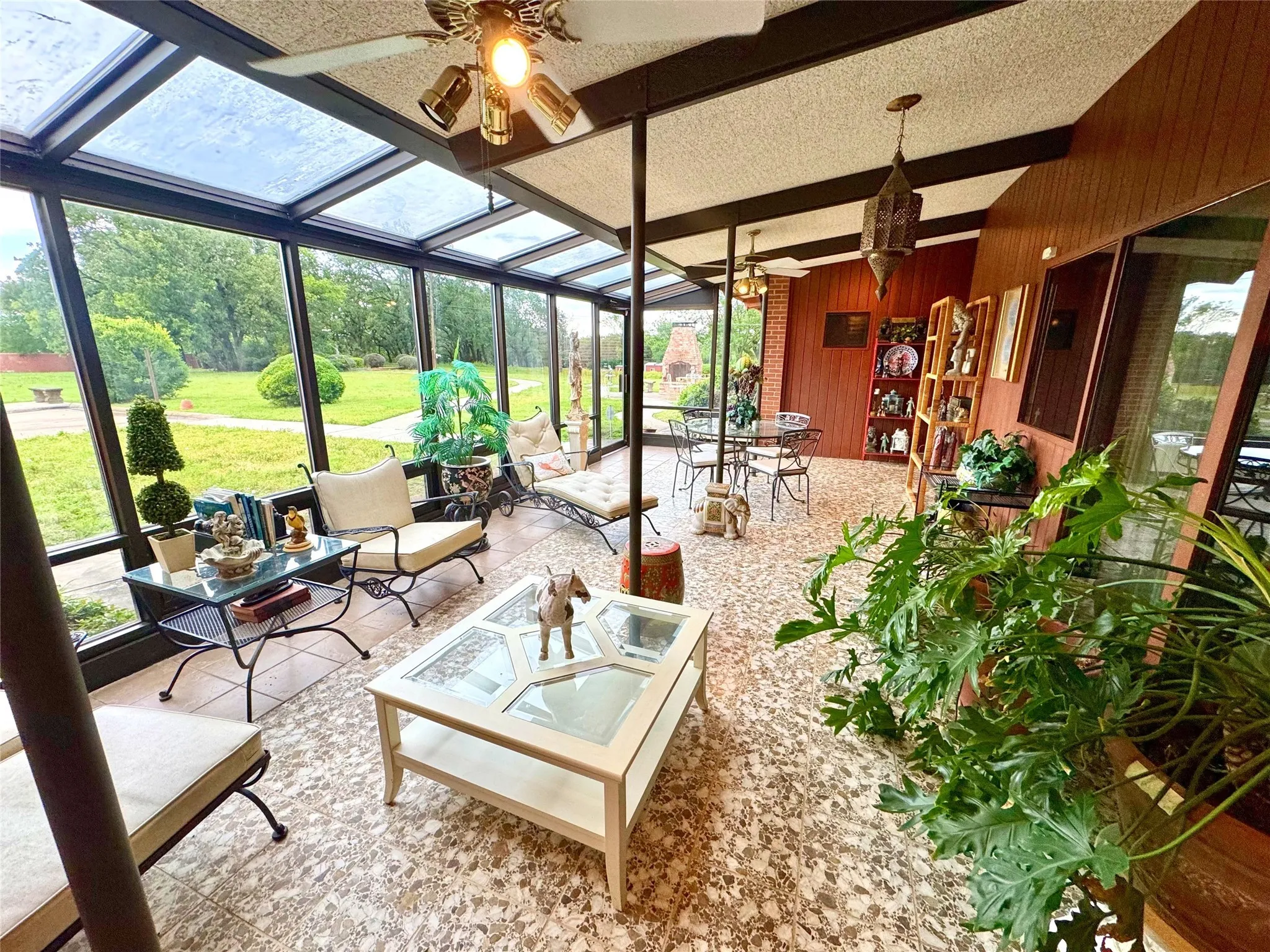Sunroom featuring outdoor dining area, ceiling fan, beam ceiling, a fire pit, and view of scattered trees