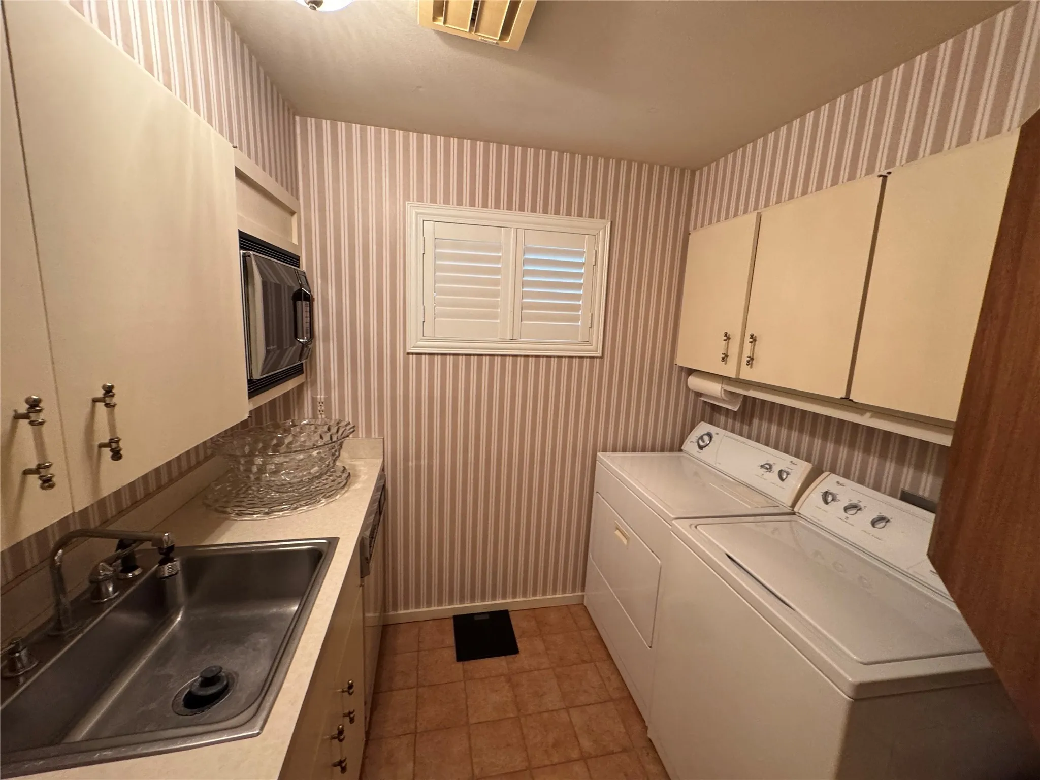 Washroom featuring wallpapered walls, independent washer and dryer, and light tile patterned flooring