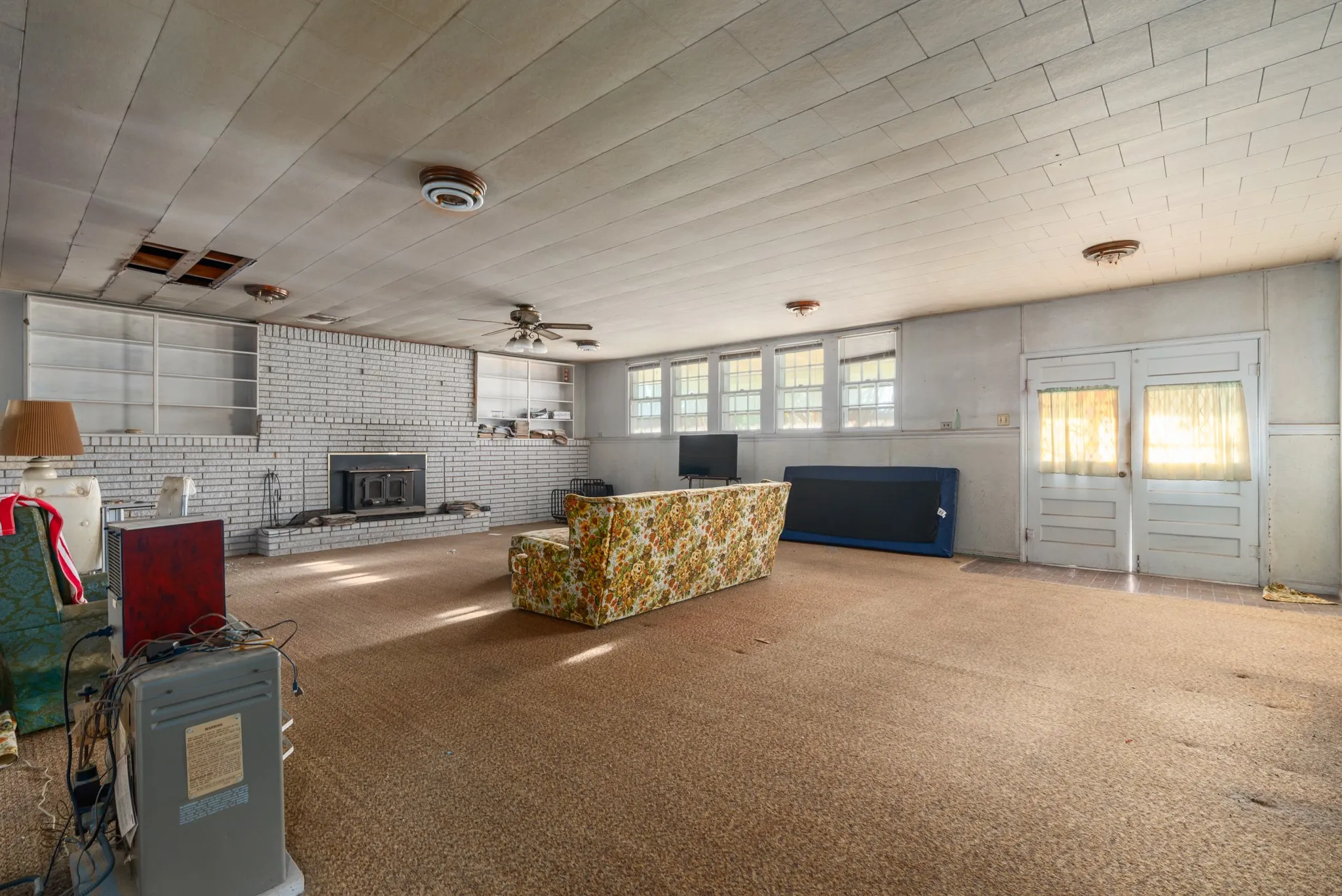 Carpeted living room with brick wall, a ceiling fan, and a wood stove