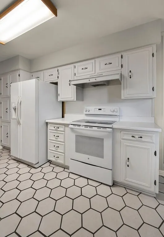 Kitchen with white appliances, under cabinet range hood, white cabinets, light countertops, and light flooring