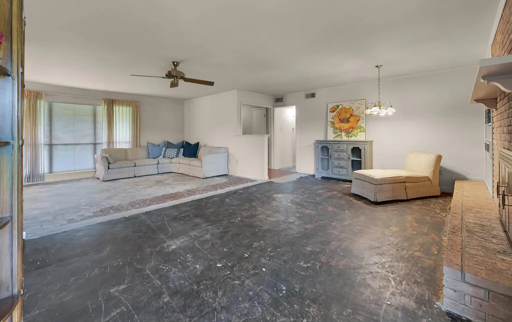 Living room featuring a fireplace, ceiling fan, a chandelier, and concrete flooring