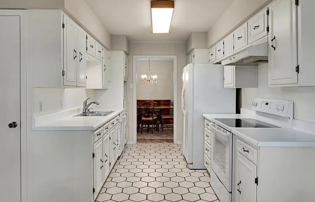 Kitchen featuring white electric range, under cabinet range hood, a sink, a chandelier, and light countertops