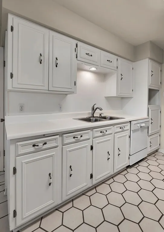 Kitchen with dishwasher, a sink, white cabinetry, and light countertops
