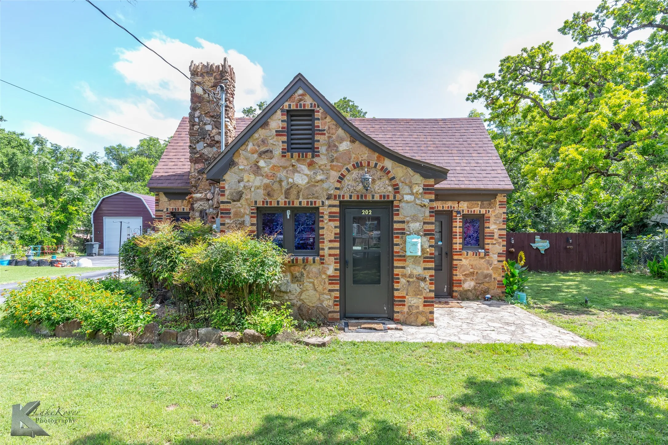 Tudor-style house featuring stone siding, a chimney, a shingled roof, and an outbuilding