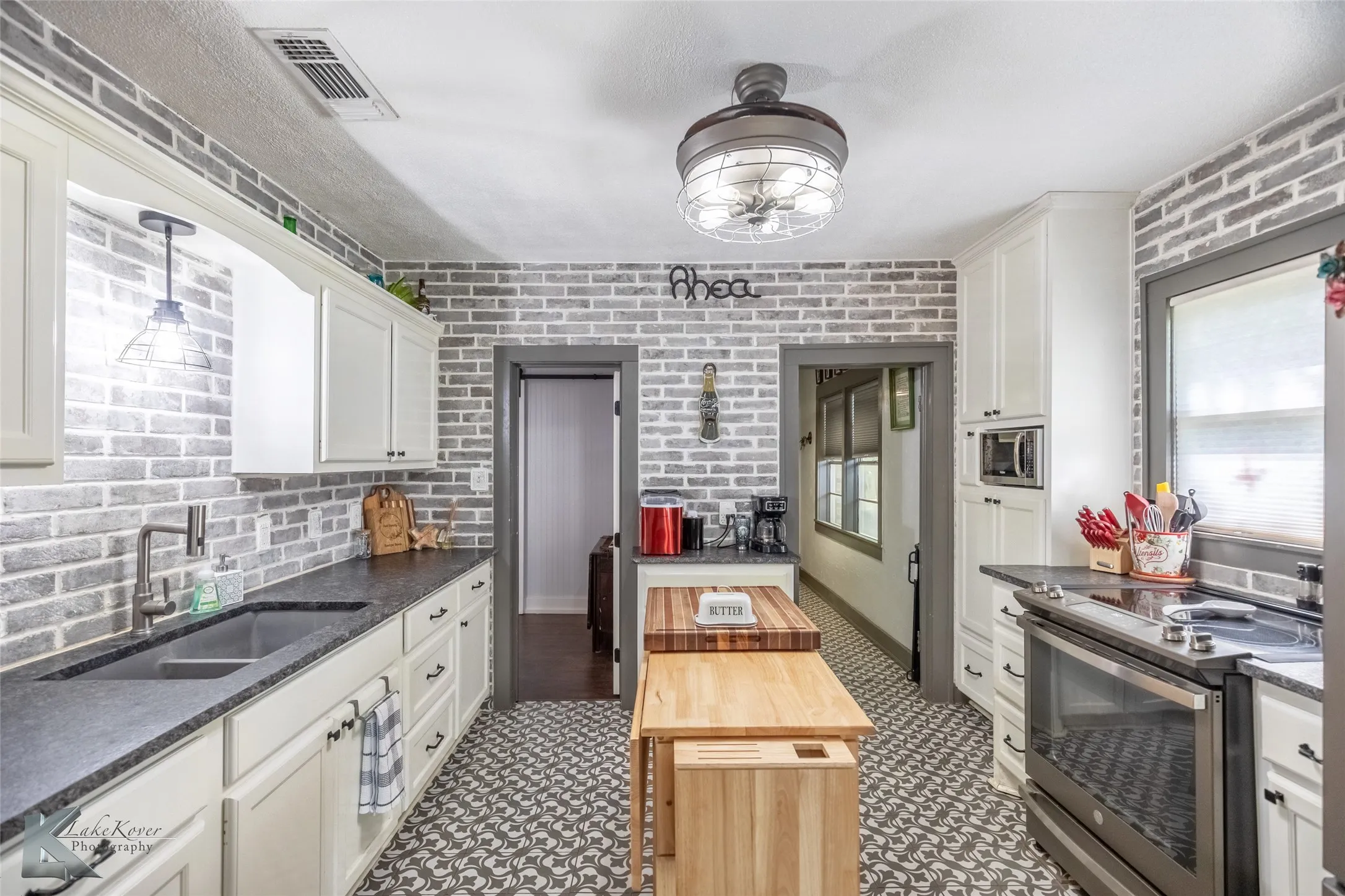 Kitchen with appliances with stainless steel finishes, a sink, white cabinets, brick wall, and dark stone counters
