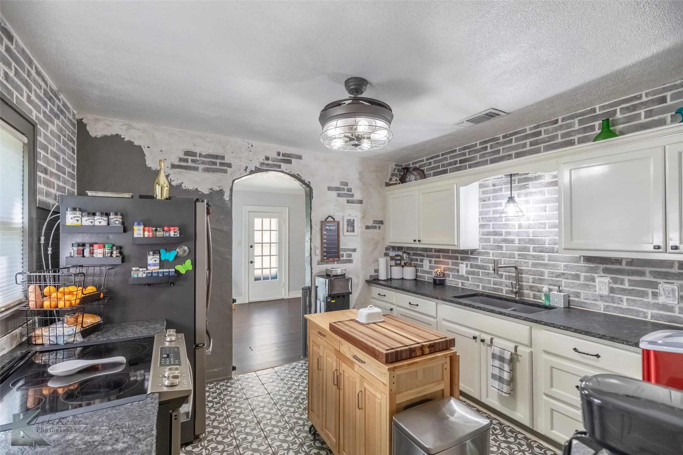 Kitchen with arched walkways, a sink, wood counters, freestanding refrigerator, and white cabinets