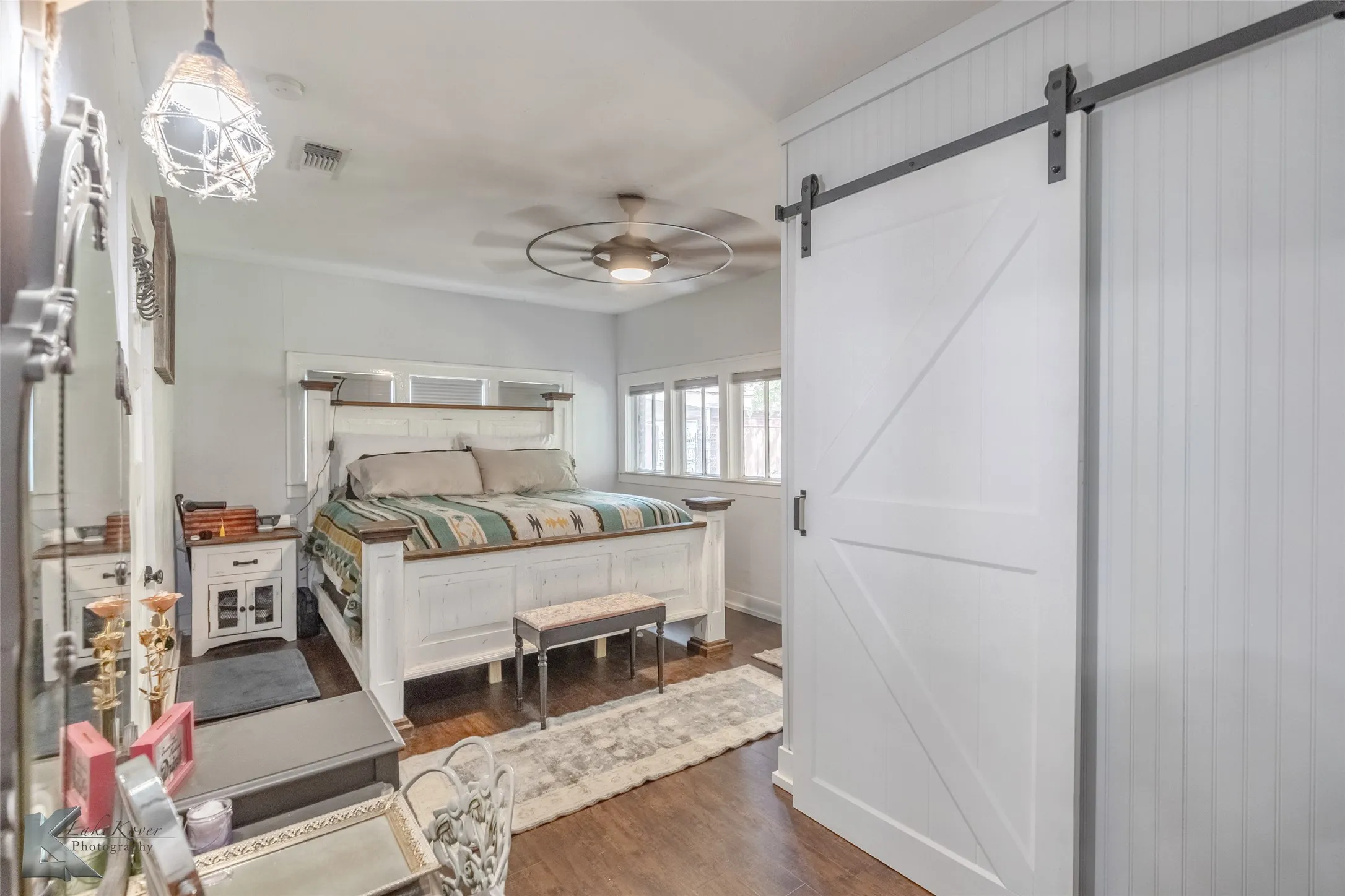 Bedroom with a barn door, dark wood finished floors, and a ceiling fan