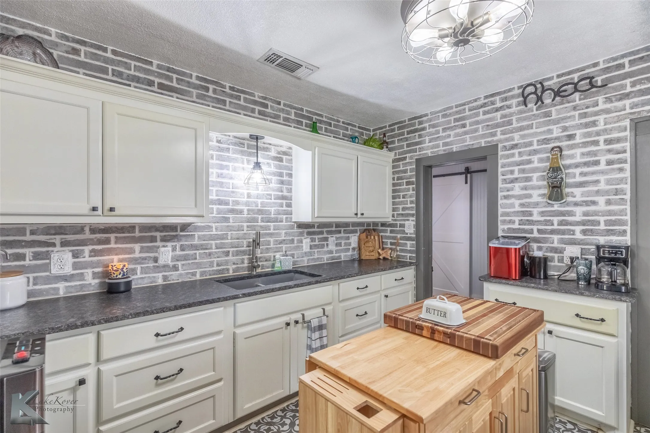Kitchen featuring a sink, wooden counters, white cabinetry, brick wall, and a barn door