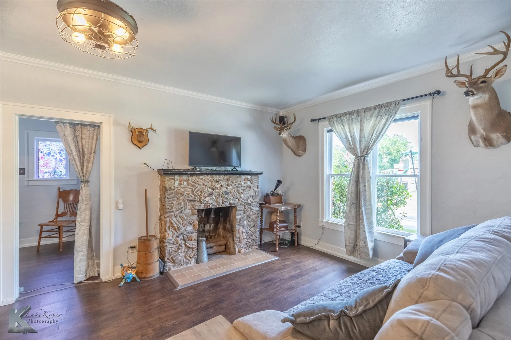 Living area with plenty of natural light, crown molding, wood finished floors, baseboards, and a stone fireplace